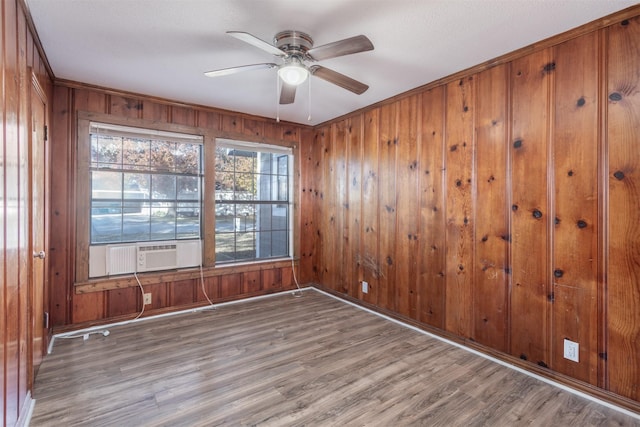 unfurnished room featuring cooling unit, ceiling fan, wood-type flooring, and wooden walls