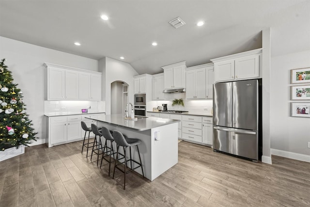 kitchen with a kitchen breakfast bar, an island with sink, stainless steel appliances, decorative backsplash, and white cabinets