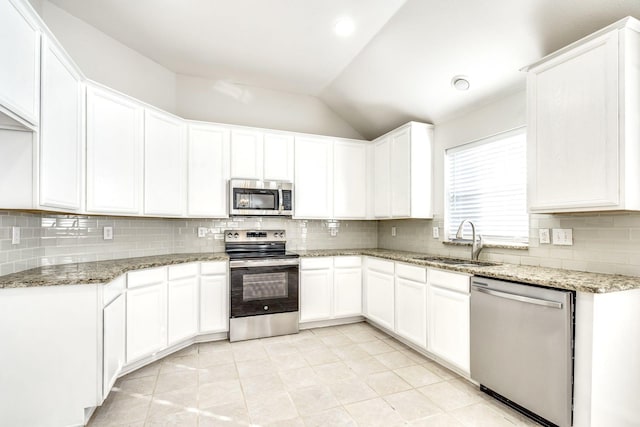 kitchen featuring lofted ceiling, sink, appliances with stainless steel finishes, light stone counters, and white cabinetry