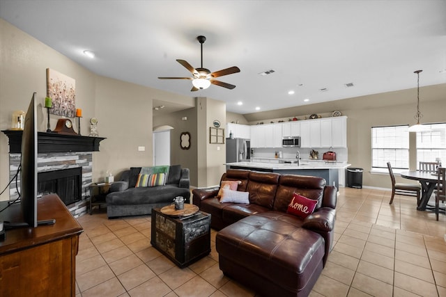 tiled living room featuring ceiling fan, a stone fireplace, and sink