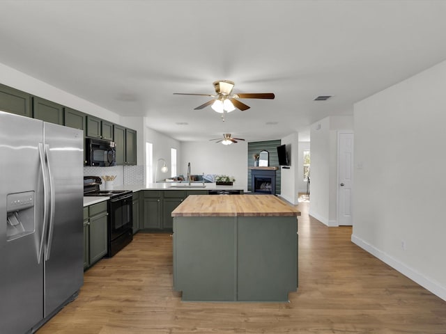 kitchen featuring kitchen peninsula, light wood-type flooring, backsplash, black appliances, and butcher block countertops