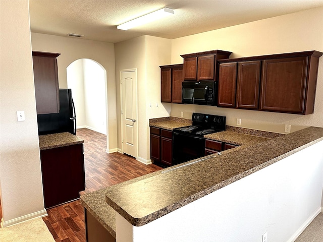 kitchen featuring black appliances, dark hardwood / wood-style floors, kitchen peninsula, and a textured ceiling