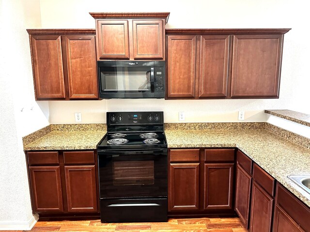 kitchen with light hardwood / wood-style floors, light stone counters, and black appliances