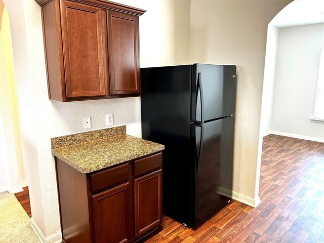 kitchen featuring black refrigerator, light stone countertops, and dark wood-type flooring