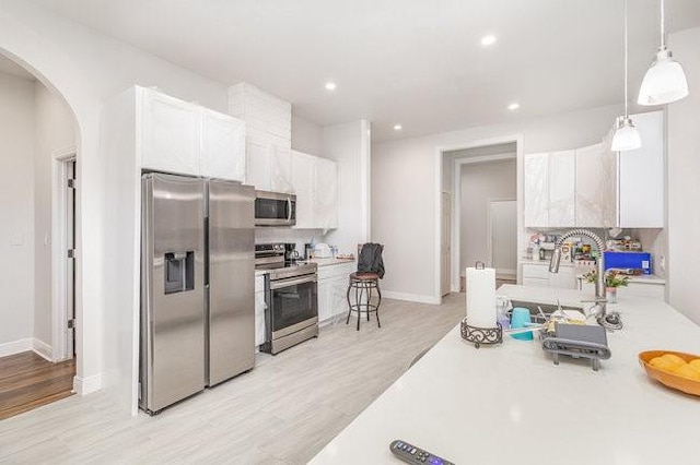 kitchen with white cabinets, pendant lighting, stainless steel appliances, and light hardwood / wood-style floors