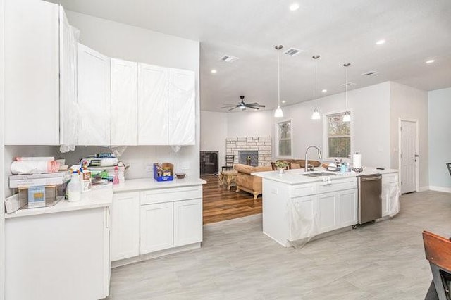 kitchen featuring ceiling fan, sink, hanging light fixtures, a fireplace, and white cabinets