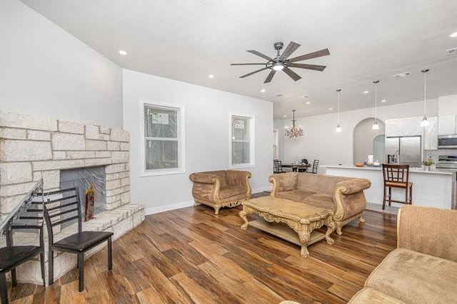 living room with ceiling fan with notable chandelier, wood-type flooring, and a fireplace