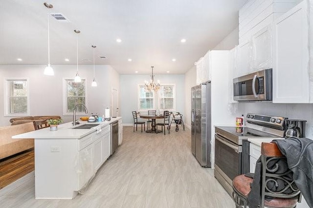 kitchen featuring white cabinetry, sink, decorative light fixtures, a center island with sink, and appliances with stainless steel finishes