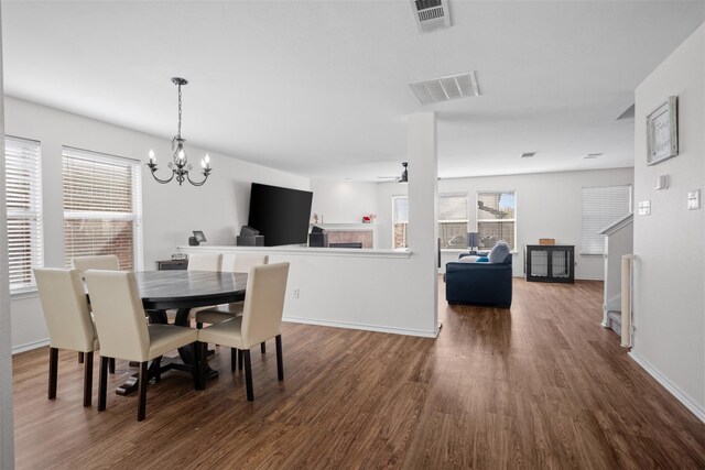 dining space featuring dark hardwood / wood-style floors, a tiled fireplace, and ceiling fan with notable chandelier