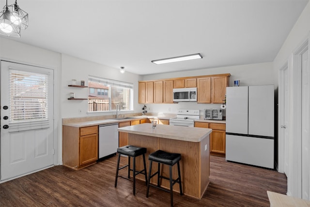 kitchen featuring sink, white appliances, a breakfast bar area, dark wood-type flooring, and a center island