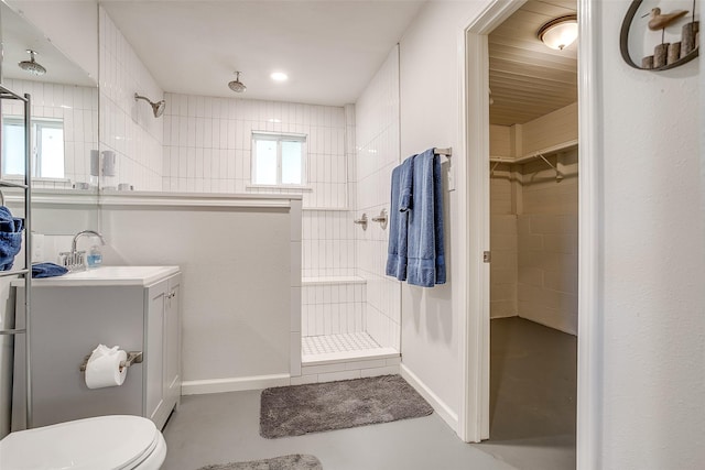 bathroom featuring vanity, toilet, a tile shower, and concrete floors