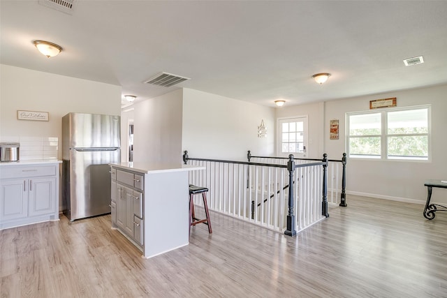 kitchen featuring gray cabinetry, a center island, light hardwood / wood-style flooring, a kitchen bar, and stainless steel refrigerator