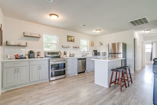 kitchen featuring a center island, stainless steel appliances, tasteful backsplash, light hardwood / wood-style flooring, and a kitchen bar