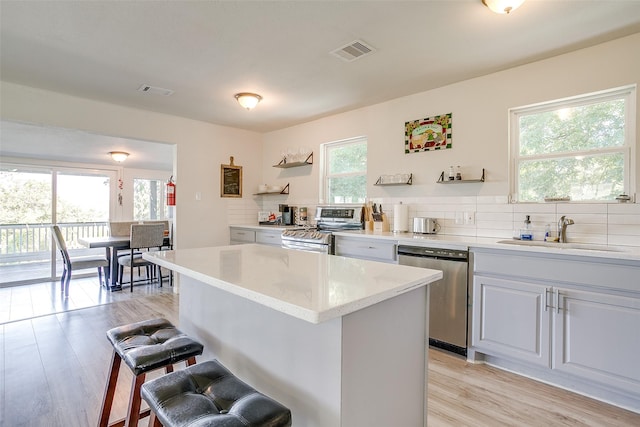 kitchen with sink, stainless steel appliances, light hardwood / wood-style floors, decorative backsplash, and a kitchen island