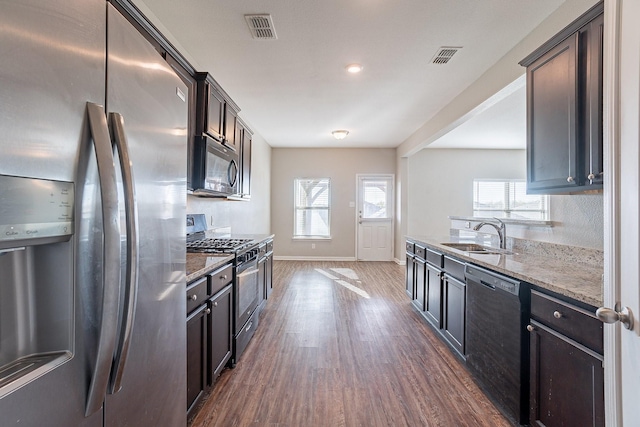 kitchen featuring light stone countertops, appliances with stainless steel finishes, dark brown cabinets, dark wood-type flooring, and sink