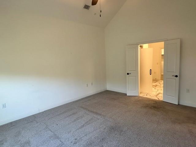 empty room featuring ceiling fan, high vaulted ceiling, and carpet