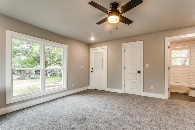 unfurnished bedroom with ensuite bath, ceiling fan, carpet floors, and multiple windows