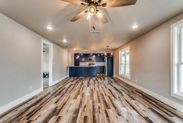 unfurnished living room featuring hardwood / wood-style flooring, ceiling fan with notable chandelier, and a healthy amount of sunlight