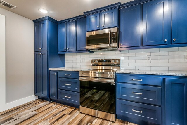 kitchen with light stone countertops, light wood-type flooring, blue cabinets, and stainless steel appliances