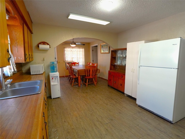 kitchen with ceiling fan, sink, wood-type flooring, a textured ceiling, and white appliances