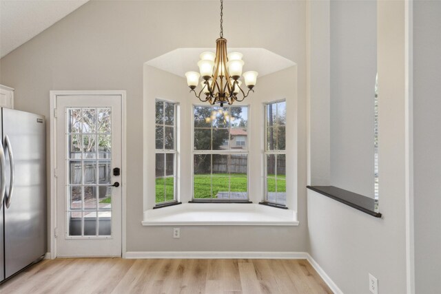 doorway featuring a notable chandelier, light wood-type flooring, and lofted ceiling