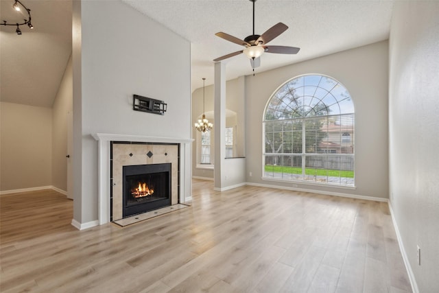 unfurnished living room with a fireplace, ceiling fan with notable chandelier, a textured ceiling, and light wood-type flooring