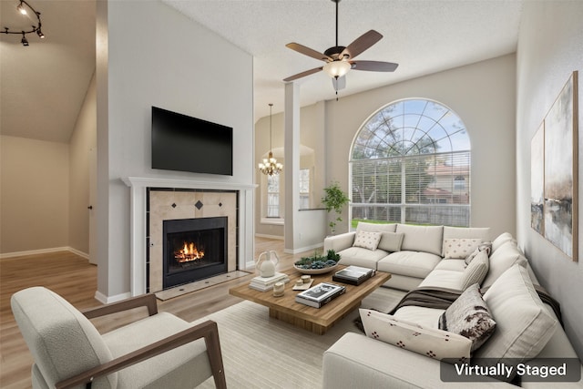 living room with high vaulted ceiling, light hardwood / wood-style floors, a textured ceiling, and a tile fireplace