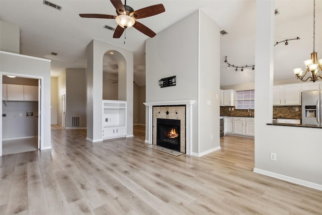 unfurnished living room featuring light wood-type flooring, ceiling fan with notable chandelier, sink, high vaulted ceiling, and a tiled fireplace