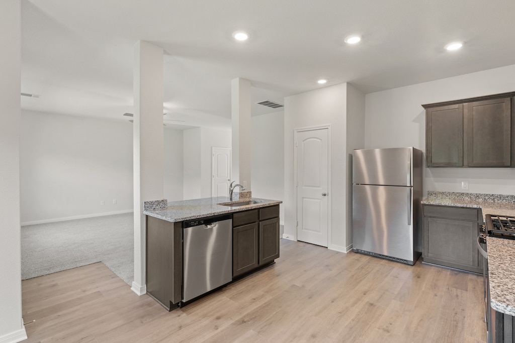 kitchen with light wood-type flooring, light stone countertops, sink, and appliances with stainless steel finishes