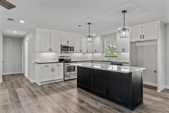 kitchen with sink, white cabinetry, a center island, hanging light fixtures, and stainless steel appliances