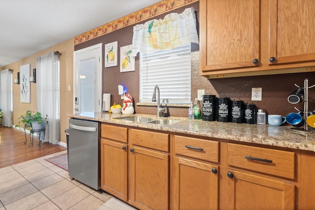 kitchen featuring a sink, light tile patterned floors, stainless steel dishwasher, and light stone countertops