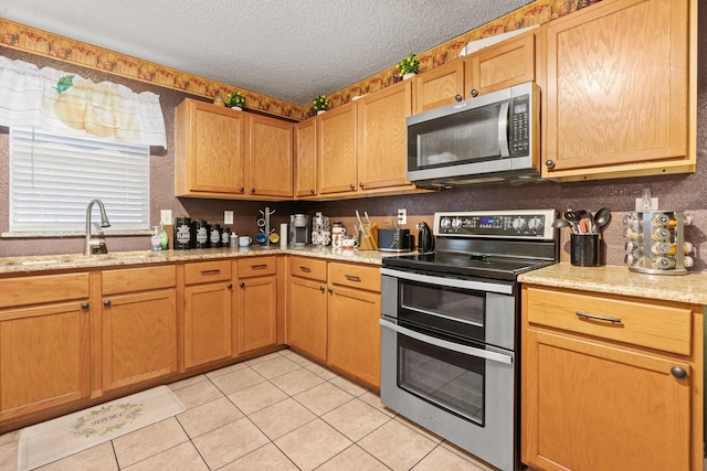 kitchen with appliances with stainless steel finishes, light stone countertops, a textured ceiling, a sink, and light tile patterned flooring