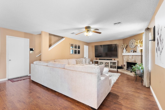 living area with baseboards, dark wood finished floors, a ceiling fan, a textured ceiling, and a fireplace