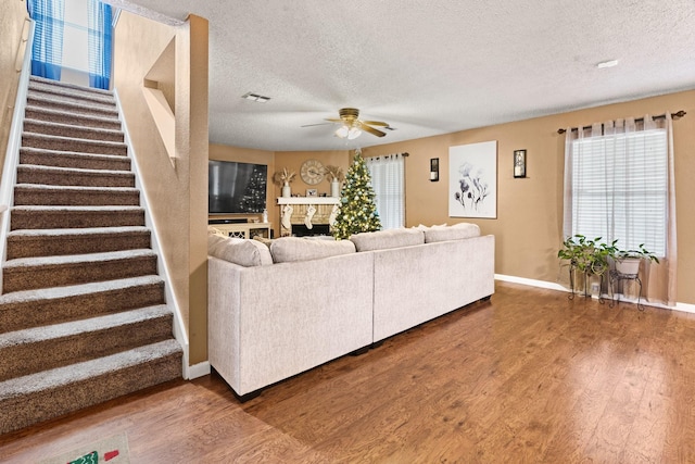 living area featuring a textured ceiling, stairs, a fireplace, and wood finished floors