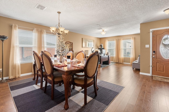 dining area with baseboards, visible vents, wood finished floors, an inviting chandelier, and a textured ceiling