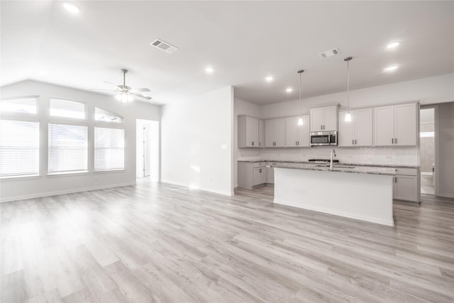 kitchen featuring light stone countertops, ceiling fan, hanging light fixtures, light hardwood / wood-style flooring, and a kitchen island with sink