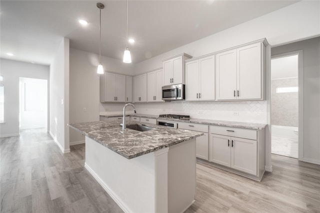 kitchen with a kitchen island with sink, sink, dark stone counters, and appliances with stainless steel finishes