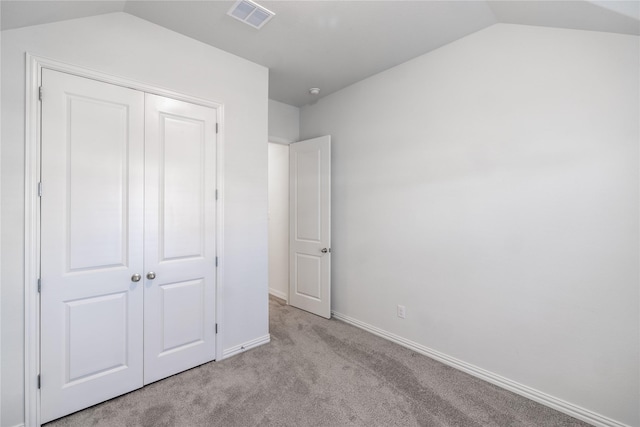 unfurnished bedroom featuring light carpet, a closet, and lofted ceiling