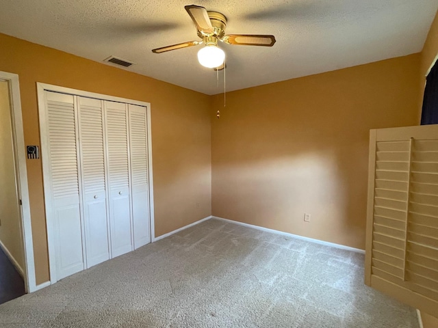 unfurnished bedroom with carpet flooring, ceiling fan, a closet, and a textured ceiling