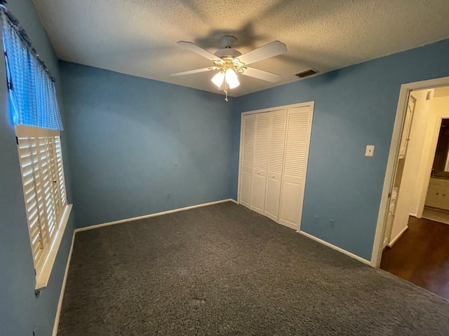 unfurnished bedroom with dark colored carpet, ceiling fan, a textured ceiling, and a closet