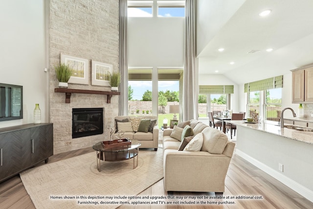 living room featuring a stone fireplace, sink, high vaulted ceiling, and light hardwood / wood-style flooring