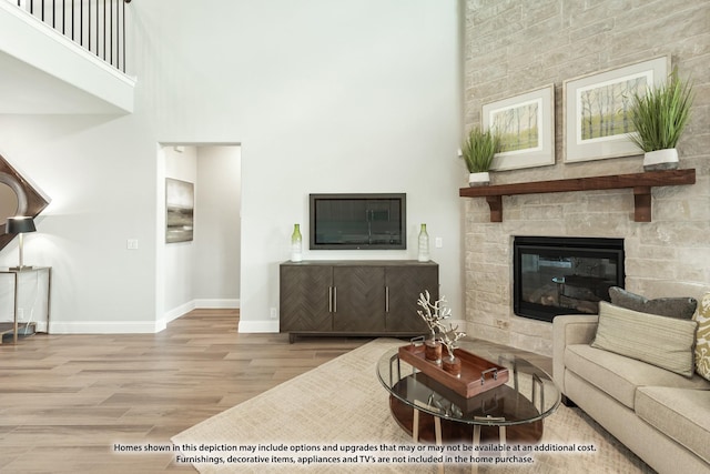 living room with a stone fireplace, a towering ceiling, and hardwood / wood-style flooring