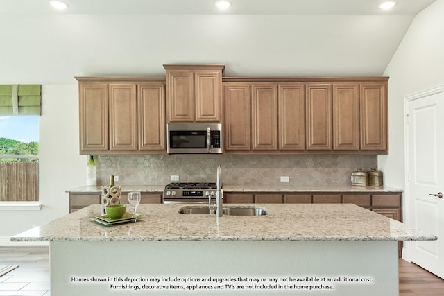 kitchen with sink, vaulted ceiling, decorative backsplash, a center island with sink, and appliances with stainless steel finishes