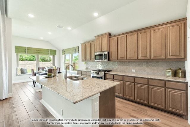 kitchen featuring sink, stainless steel appliances, light hardwood / wood-style flooring, an island with sink, and vaulted ceiling