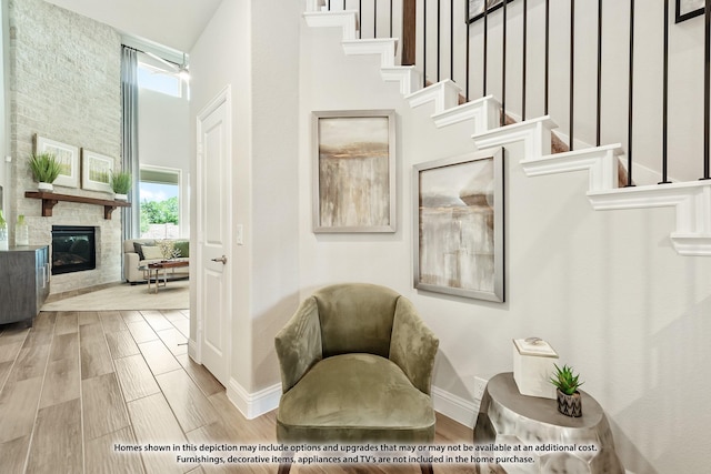 sitting room with a fireplace, a towering ceiling, a healthy amount of sunlight, and light wood-type flooring