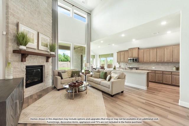 living room featuring a stone fireplace, light wood-type flooring, sink, and a towering ceiling