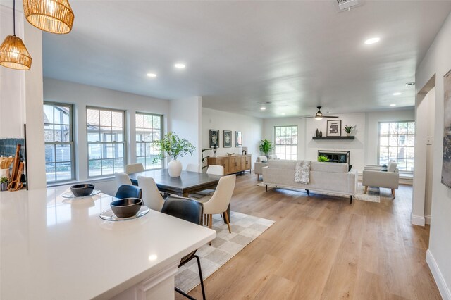 dining space with ceiling fan, plenty of natural light, a fireplace, and light hardwood / wood-style flooring