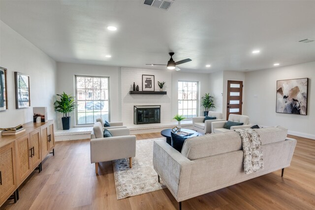 living room with a brick fireplace, ceiling fan with notable chandelier, and light hardwood / wood-style flooring