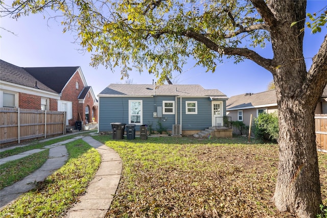 rear view of property featuring central air condition unit and a lawn