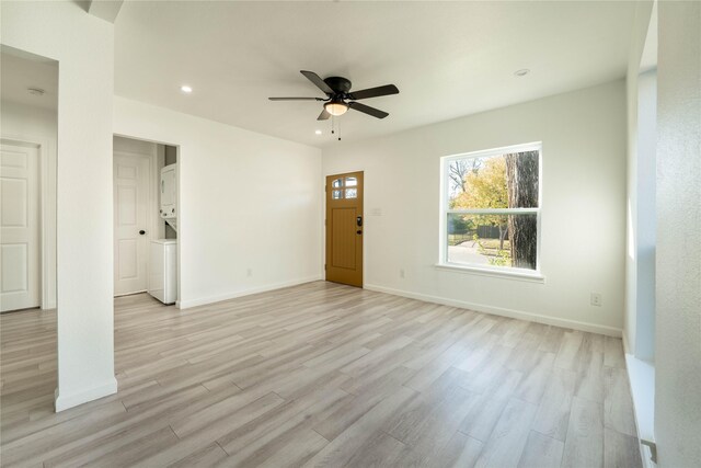 spare room featuring ceiling fan, stacked washer and dryer, and light hardwood / wood-style flooring